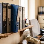 A closed binder on a shelf above an office desk.