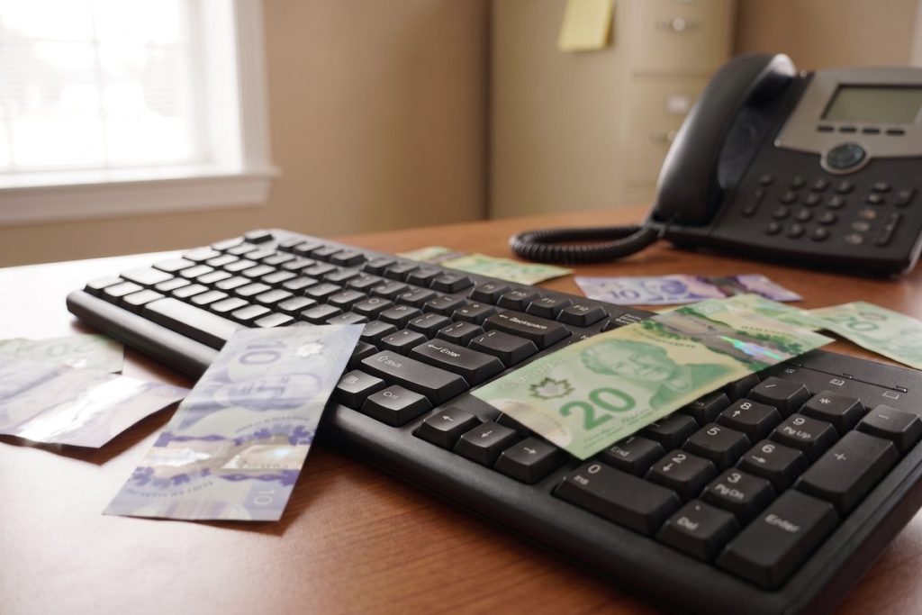 Canadian banknotes scattered across a keyboard and desk in an office.